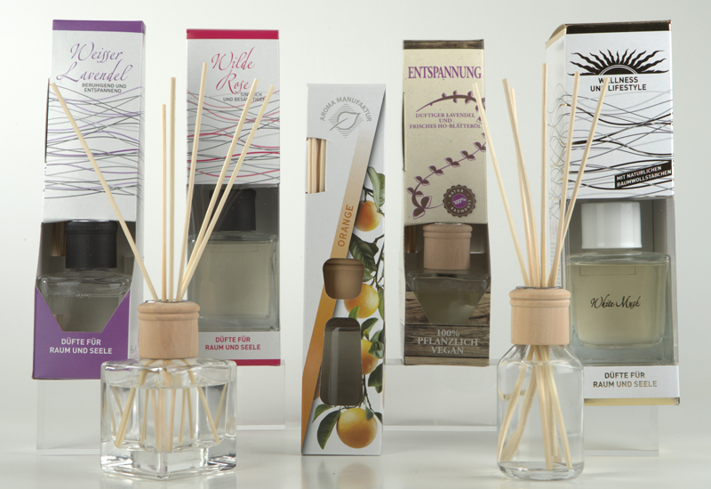 Verschiedene Raumduft-Sets mit Diffuser-Fl&auml;schchen, Holzst&auml;bchen und den dazugeh&ouml;rigen Produktverpackungen stehen nebeneinander auf hellem Hintergrund.