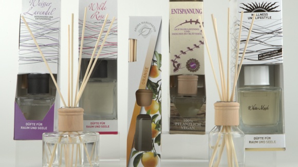 Eine Auswahl verschiedenster Aromadiffuser im Glasflakon mit Rattanst&auml;bchen inklusive Verpackungen auf hellem Hintergrund